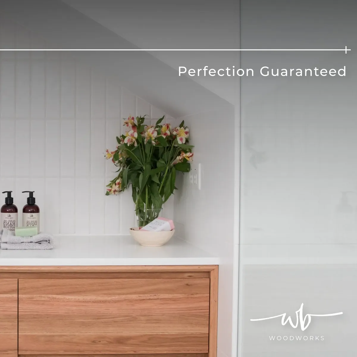 Warm timber bathroom vanity drawer under a white countertop with a vase of flowers and vertical white tiles